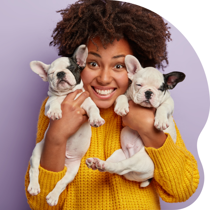 A person smiling and holding two puppies up to her face.